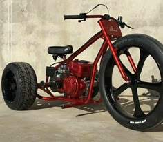 a red motorcycle parked in front of a cement wall with black spokes and wheels