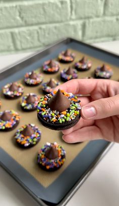 a hand holding a chocolate covered donut with sprinkles on it in front of a baking sheet