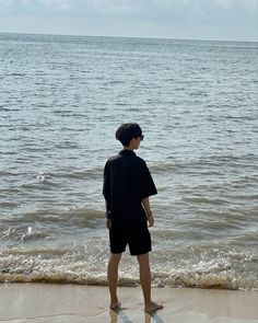 a boy standing on the beach looking out at the water