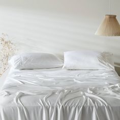 an unmade bed with white sheets and pillows on top of it, next to a lamp