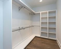 an empty walk in closet with white shelving and wood flooring on the side