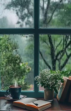 an open book on a table next to a window with rain coming down and a cup of coffee