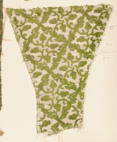 an old piece of cloth with green and white designs on it, hanging from a wall