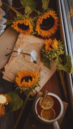 an open book with sunflowers on it next to a cup of coffee and a candle