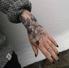 a woman's hand with black and white flowers tattooed on the left side of her arm