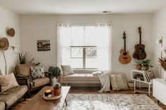 a living room filled with furniture and a guitar hanging on the wall next to a window