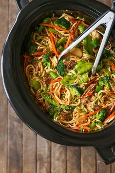 a pot filled with noodles, broccoli and carrots on top of a wooden table