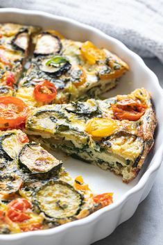 a quiche with tomatoes, zucchini and spinach in a white dish