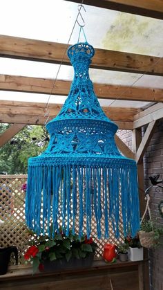 a blue crocheted chandelier hanging from a wooden ceiling in a backyard