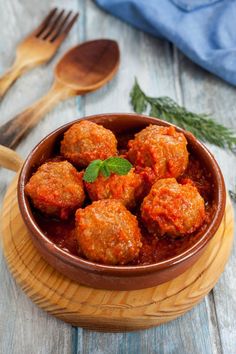 meatballs with tomato sauce in a bowl next to a wooden spoon and fork on a table