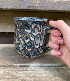 a hand holding a coffee mug on top of a wooden bench