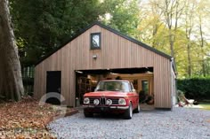 an old red truck is parked in front of a garage with its doors open and it's lights on