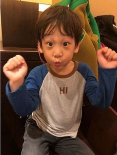 a young boy sitting on top of a wooden bench with his hands in the air