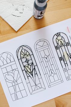 three stained glass windows sitting on top of a table next to a bottle of paint