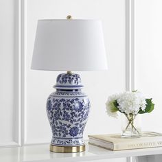 a blue and white vase sitting on top of a table next to a book with a lamp