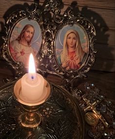 a lit candle sitting on top of a table next to two framed pictures with jesus and mary