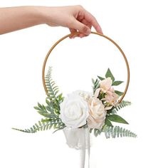 a hand holding a hoop with flowers in it and greenery on the bottom half