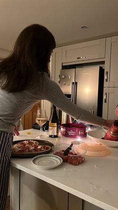 a woman standing at a kitchen counter preparing food on a pan and another person holding a knife in the other hand