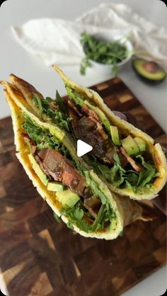 two wraps filled with meat, lettuce and other vegetables on a cutting board