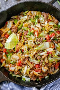 a skillet filled with ground beef, cabbage, and red peppers topped with a lime wedge