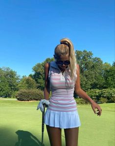 a woman in a short skirt is holding a golf club and looking down at the ground