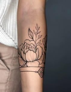 a woman's arm with a black and white flower tattoo on the left forearm