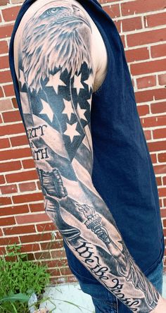 a man with an american flag and eagle tattoo on his arm is standing in front of a brick wall