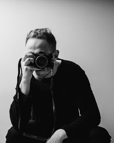 black and white photograph of a man holding a camera up to his face with both hands