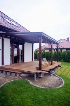 a wooden deck in front of a white house with green grass and bushes around it