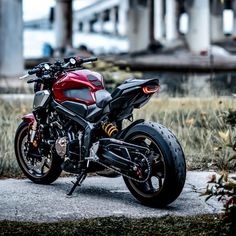 a red and black motorcycle parked on the side of a road next to tall grass