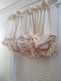 a white window with ruffled curtains hanging from it's valance in front of a window