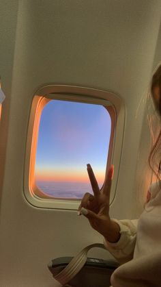 a woman sitting on an airplane with her hand up in the air while looking out the window