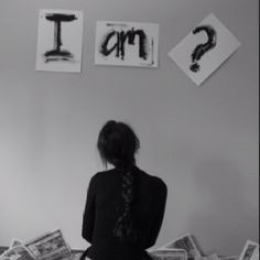 a woman standing in front of a wall with pictures on it and question mark above her head