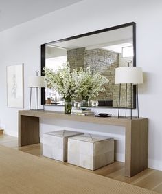 a large mirror sitting above a table with two stools and a vase filled with flowers