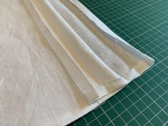 three pieces of white fabric sitting on top of a green cutting board next to a pair of scissors