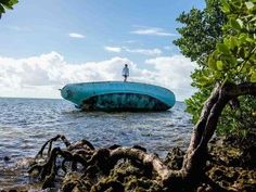 a man standing on top of a blue boat in the ocean next to rocks and trees