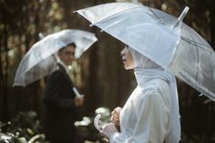 two people standing in the woods with umbrellas over their heads and one person holding an umbrella