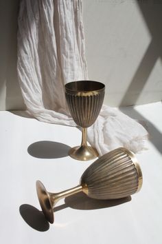 two brass goblets sitting on top of a white table