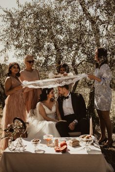 a group of people standing around a table with food on it and an umbrella over them