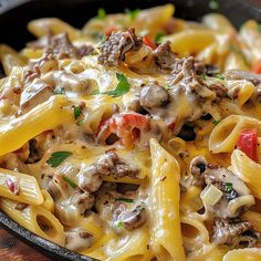 a skillet filled with pasta and meat covered in cheese sauce on top of a wooden table