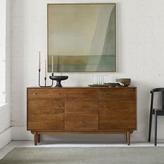 a wooden dresser sitting next to a black chair in a room with a painting on the wall