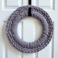 a roped wreath hanging on the front door of a white door with a black handle