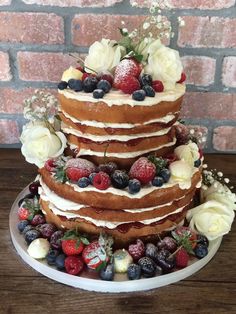 a three tiered cake with fresh berries and flowers on the top is sitting on a wooden table