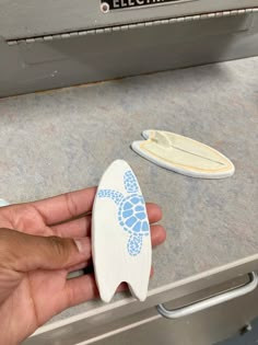 a person holding a surfboard next to some magnets on a counter top with a microwave in the background