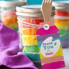 a jar filled with rainbow colored cake next to a purple towel and wooden utensils