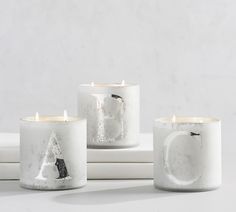 three white candles sitting next to each other on top of a table with one candle in the shape of a letter