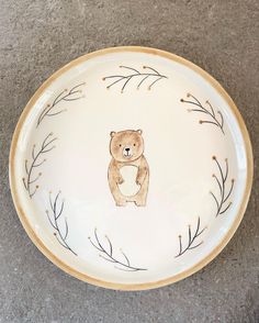 a white plate with a brown bear painted on the side and branches in the middle