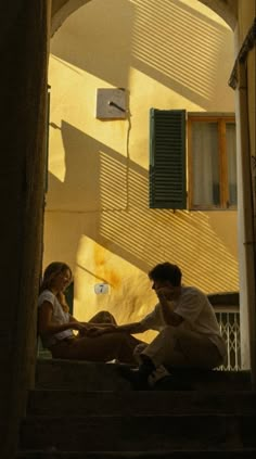 a man and woman sitting on the steps in front of a building with green shutters