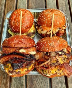 four hamburgers with meat and cheese are on a metal tray, ready to be eaten