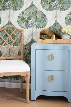 a blue dresser next to a white chair and wallpaper